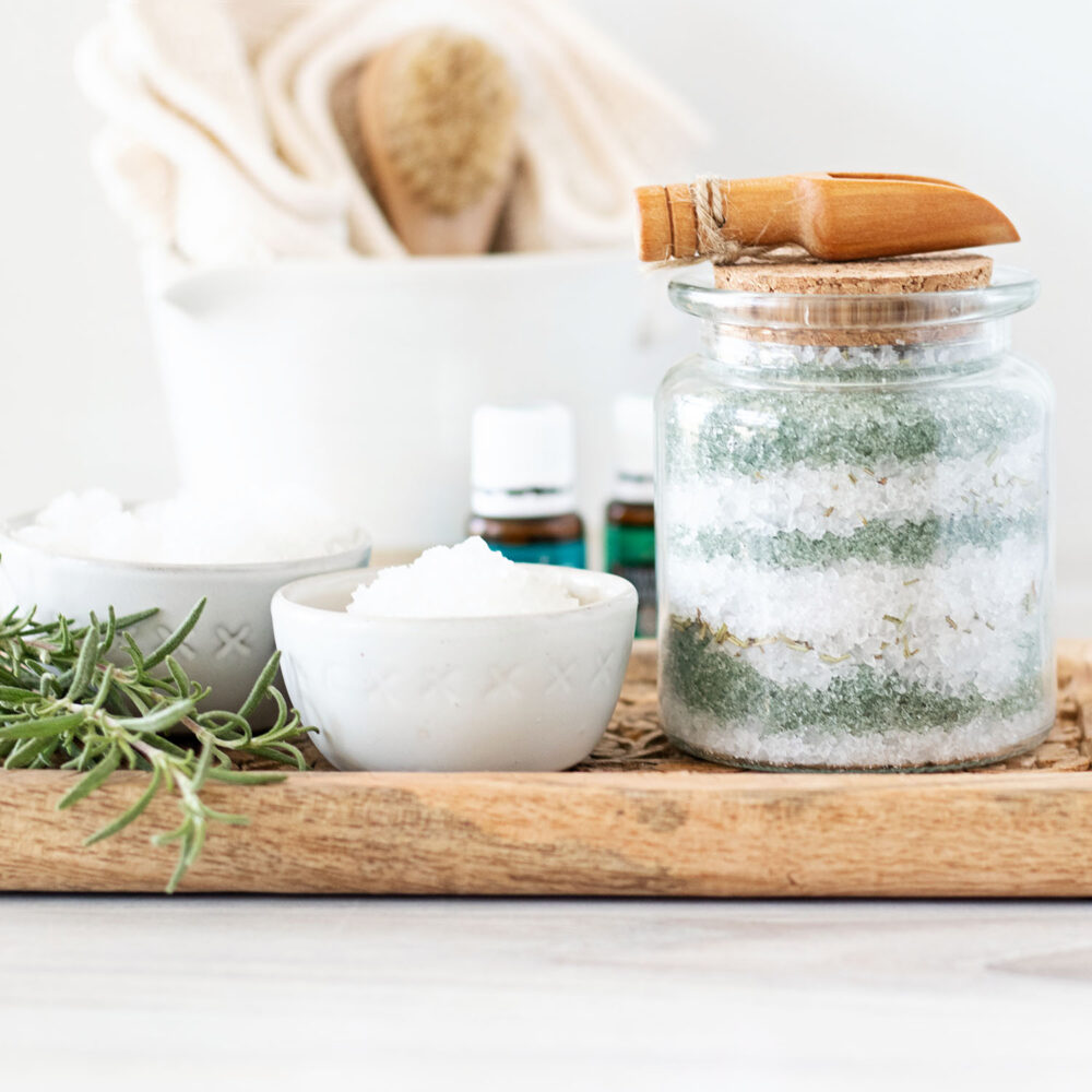 Layered jar of green and white bath salts with essential oil bottles