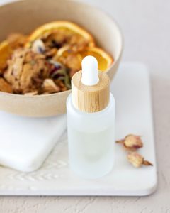 frosted glass dropper bottle filled with potpourri oil in front of a bowl of homemade potpourri