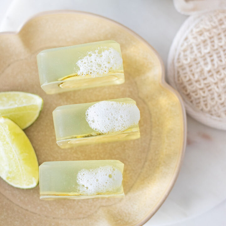 three clear aloe vera soap bars on a tray topped with suds, next to fresh lime slices