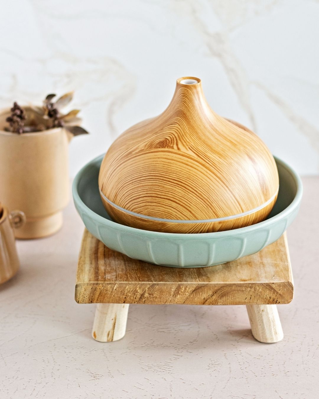 Wood diffuser in a large, turquoise ceramic bowl on top of a wooden stand on a bakery counter top.