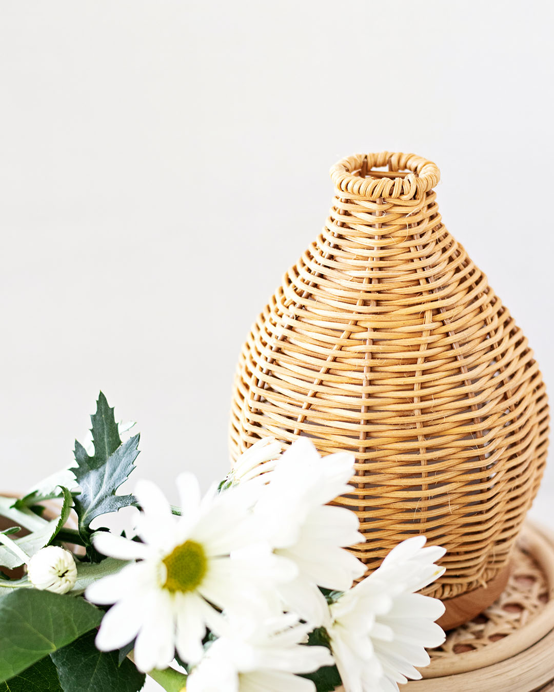 Natural rattan essential oil diffuser next to fresh picked daisy flowers.